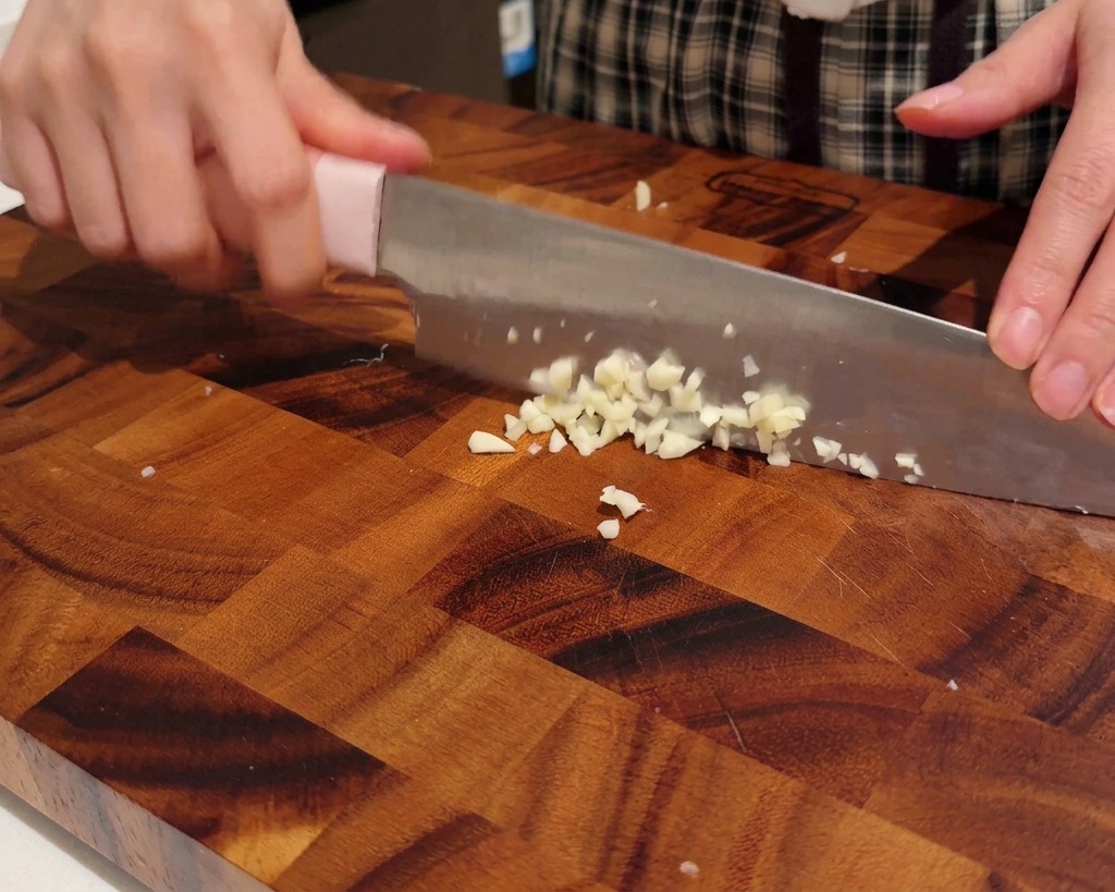 Manos picando dientes de ajo en trozos pequeños sobre una tabla de madera.
