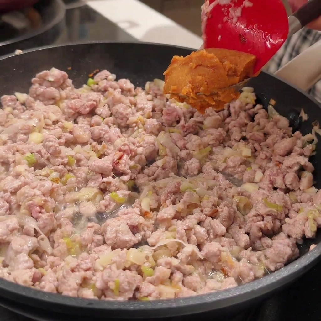 Una espátula roja sosteniendo una cucharada de pasta de miso sobre la carne dorada.