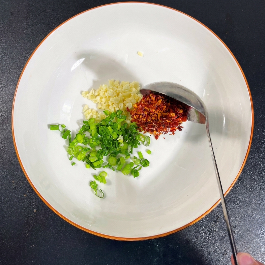 Un tazón con ajo, cebolletas y montoncitos de sal, MSG, hojuelas de chile y un chorrito de salsa de soja.