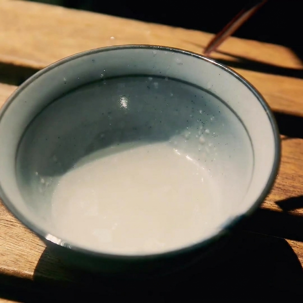 Un pequeño cuenco sobre una superficie de madera que contiene una mezcla de sake, azúcar y salsa de soja.