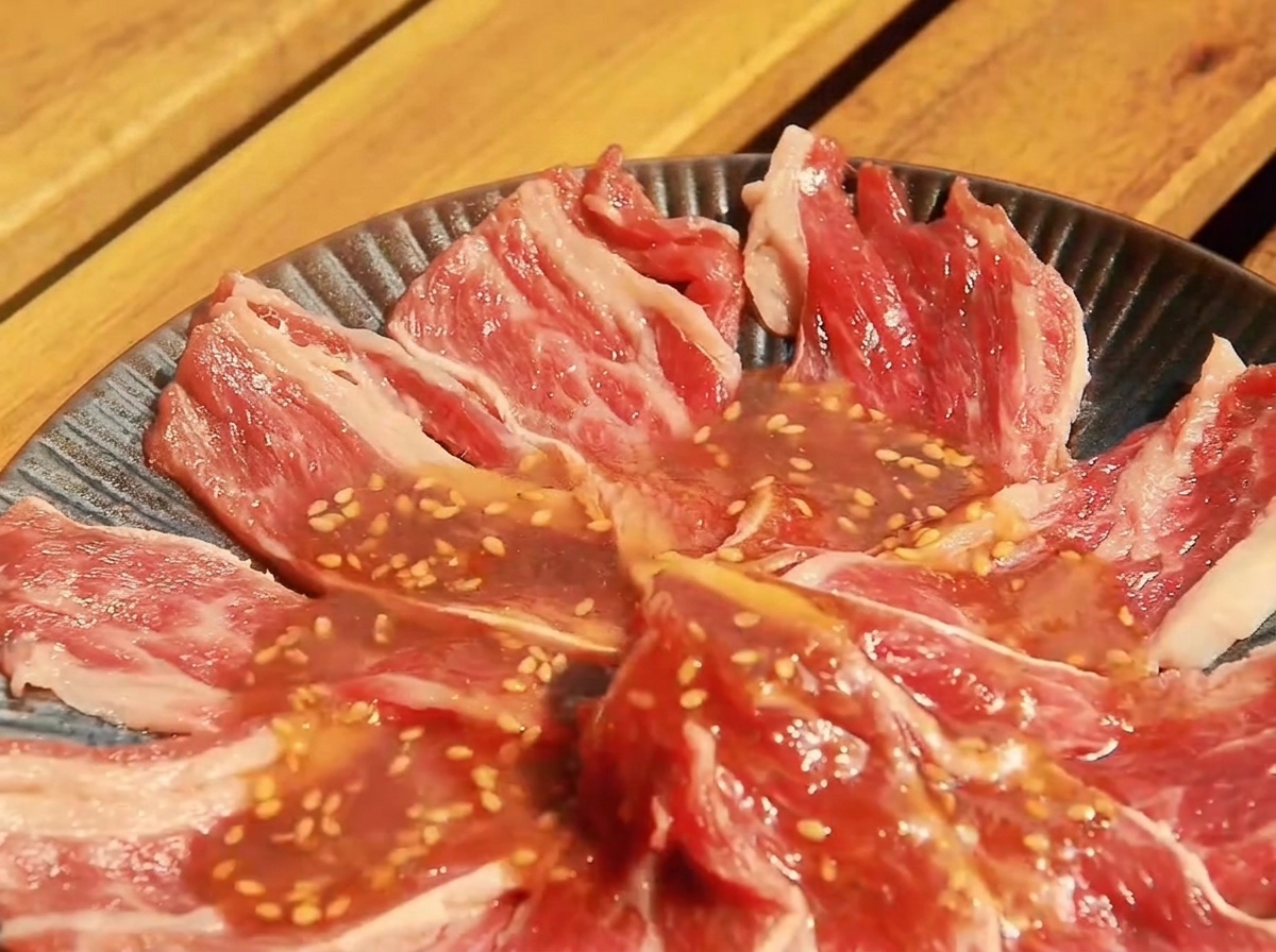 Tiras finas de ternera cruda dispuestas en un plato hondo, cubiertas con la salsa Yakiniku preparada.