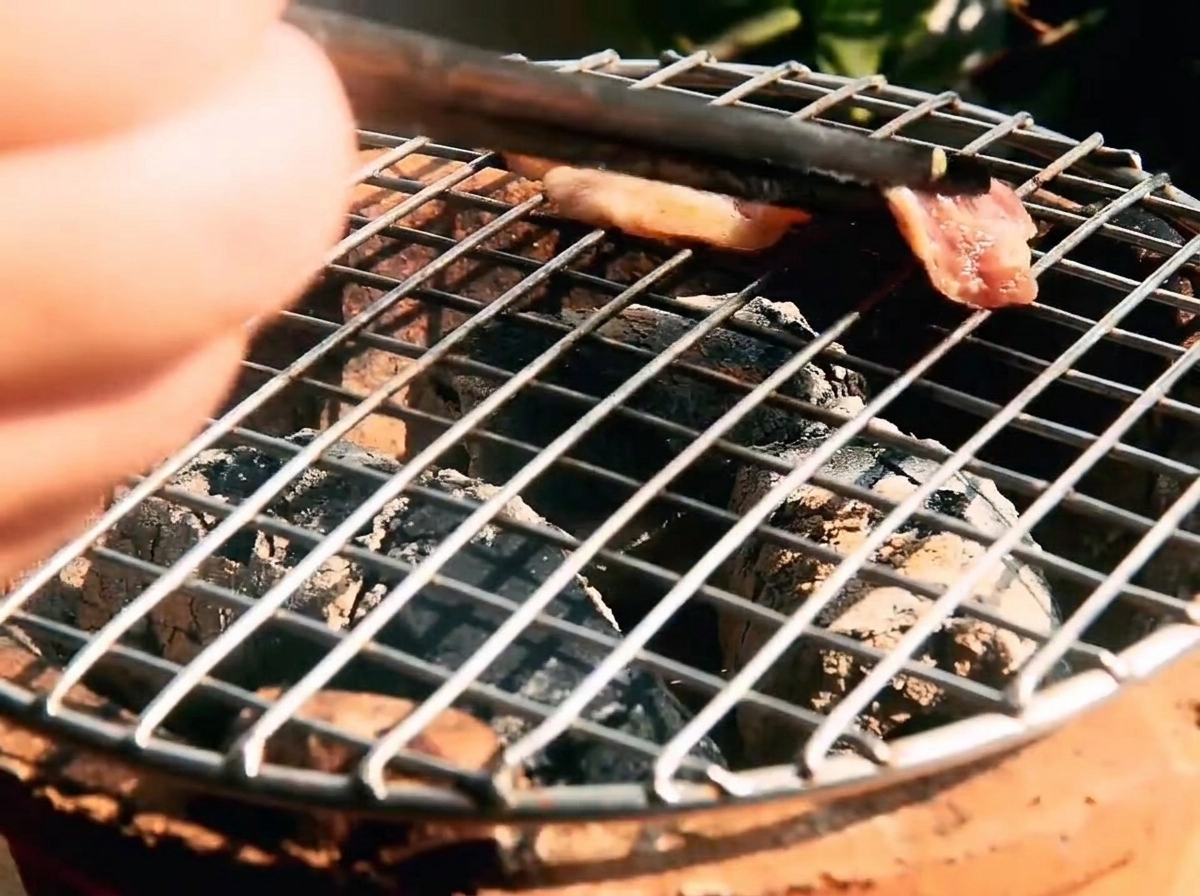 Tiras de ternera marinada cocinándose en una rejilla caliente con brasas brillantes debajo.