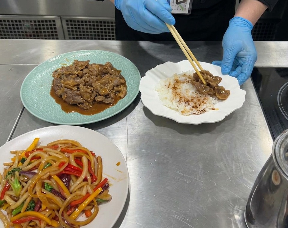 Vista en primer plano de un tazón de servir siendo rellenado con una base de arroz blanco, seguido de porciones de ternera cocinada y verduras salteadas coloridas.