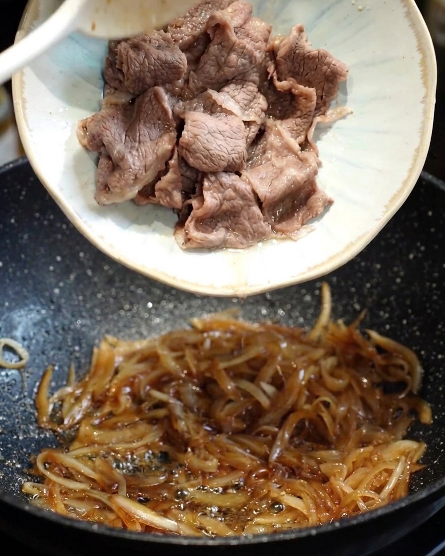 Una salsa teriyaki oscura y sabrosa vertida en la sartén con la cebolla y la ternera.