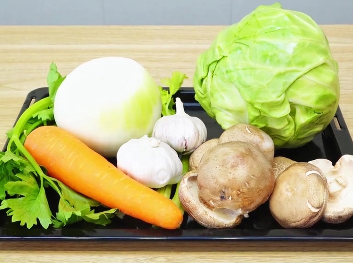 Variedad de verduras frescas incluyendo cebolla, ajo, zanahoria, apio, shiitake y repollo sobre una tabla de cortar.