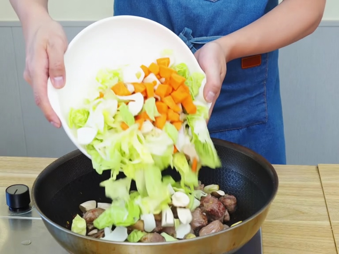 Verduras picadas y trozos de ternera salteándose juntos en una sartén grande.