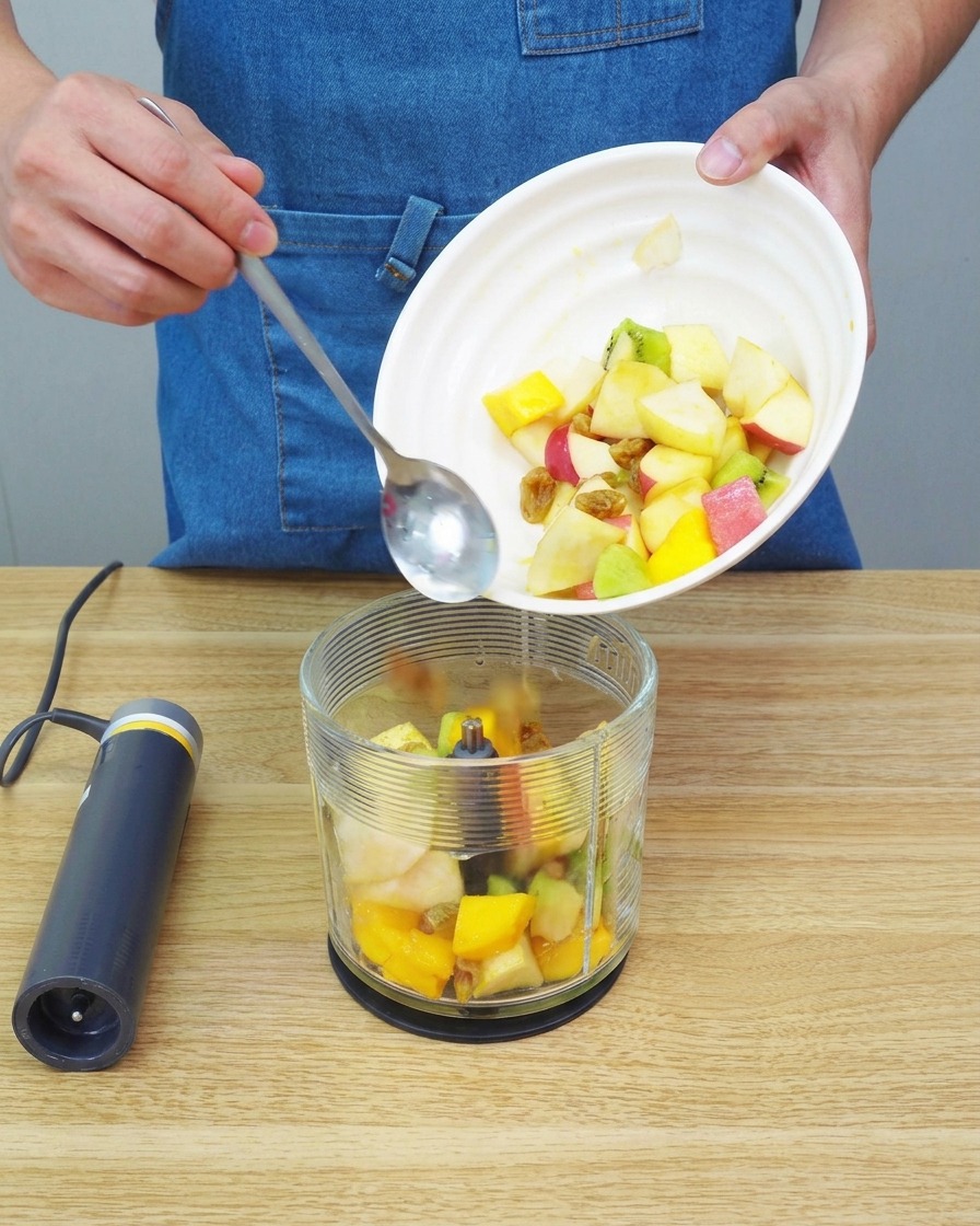 Primer plano de trozos de fruta siendo procesados hasta formar un puré suave en una batidora.