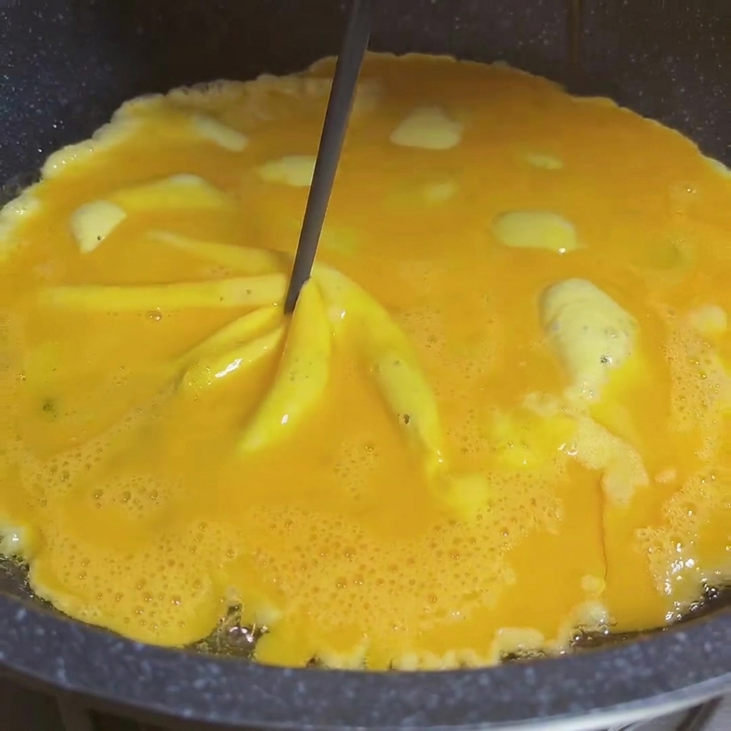 Primer plano de palillos girando huevos en la sartén creando un efecto espiral.