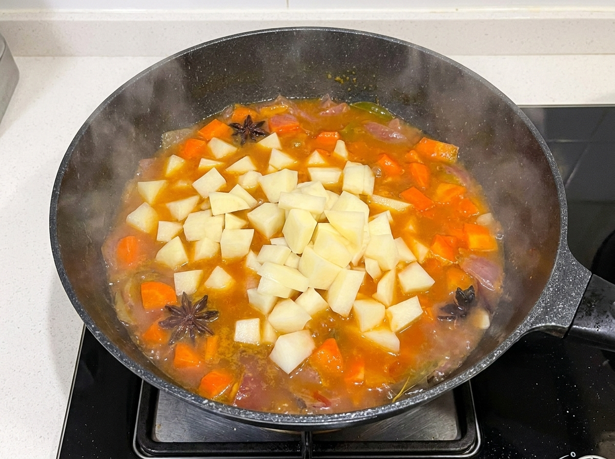 Patatas troceadas siendo añadidas a la sartén con el caldo de ternera y zanahorias.