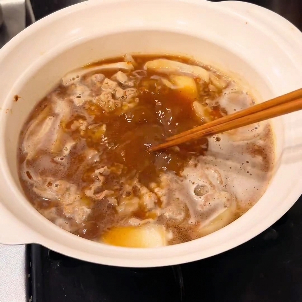 Un bloque de roux de curry siendo incorporado en la olla para crear una salsa espesa.