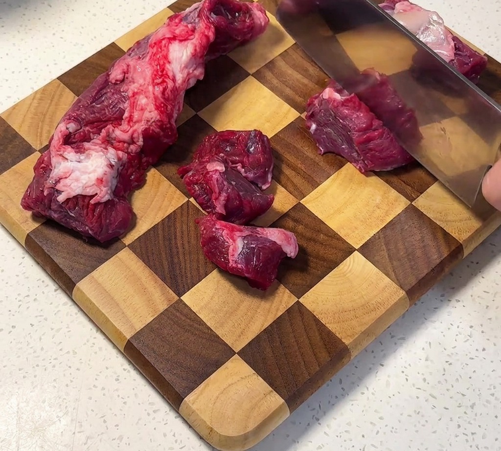 Falda de res cortada en cubos uniformes sobre una tabla de cortar de madera.