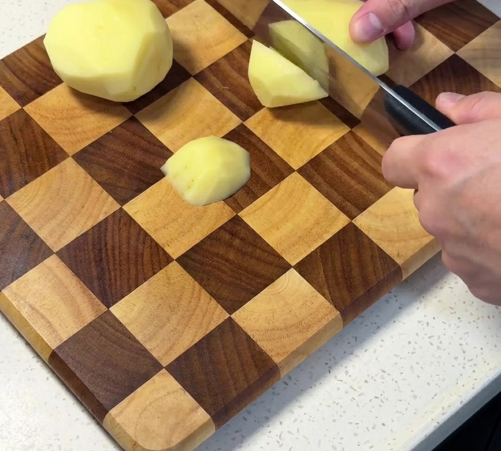 Patatas crudas peladas cortadas en cubos sobre una tabla de madera.