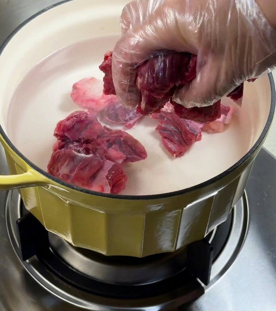 Falda de res blanqueándose en una olla con agua y aromáticos.