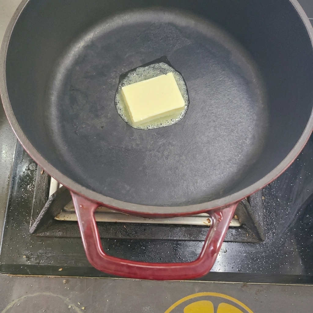 Un cubo de mantequilla derritiéndose en una olla negra sobre los fogones.