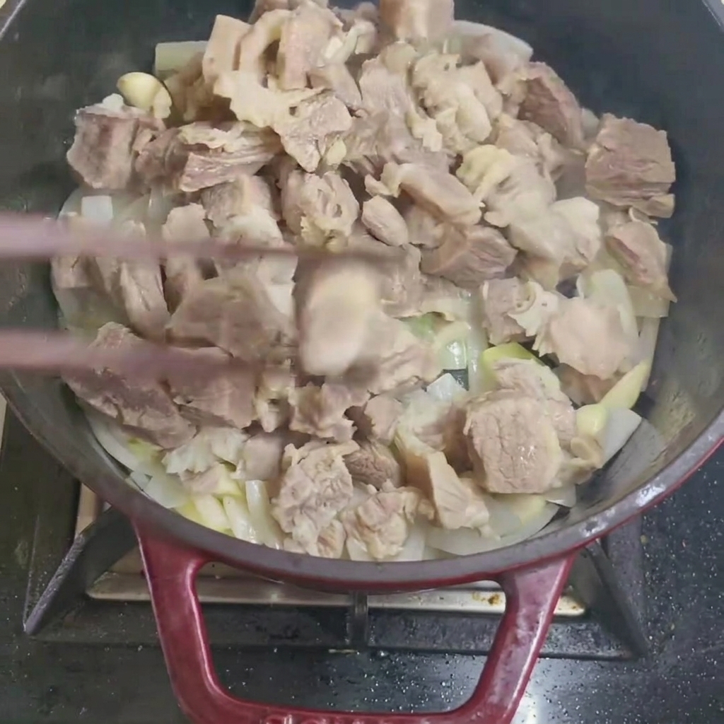Removiendo trozos de ternera blanqueados con cebolla y ajo en una olla.