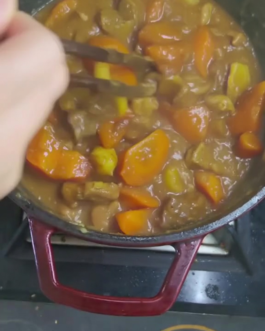 Removiendo la espesa salsa de curry con un utensilio de madera para disolver completamente las pastillas.