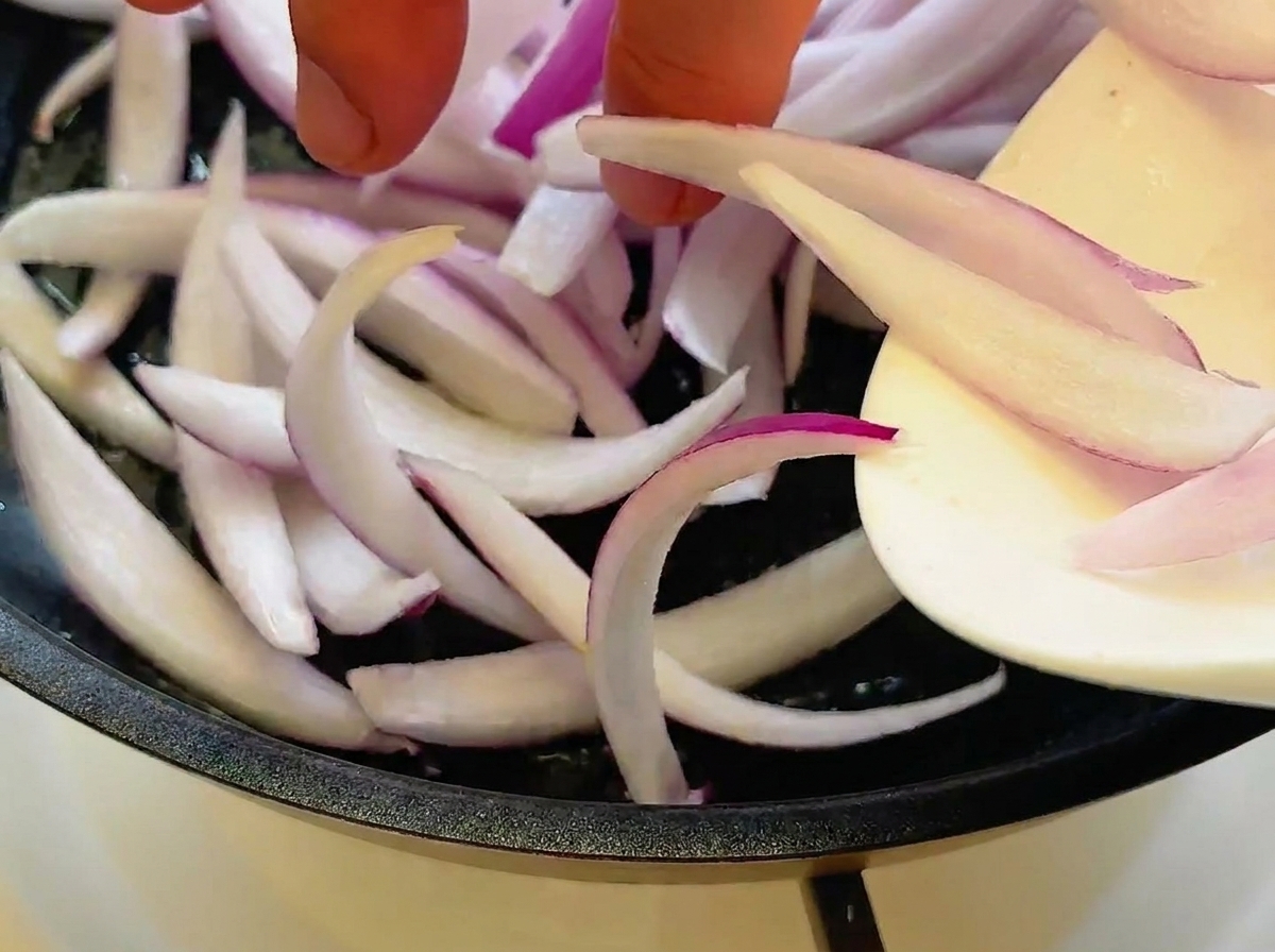 Rodajas de cebolla morada salteándose en la sartén hasta quedar translúcidas.