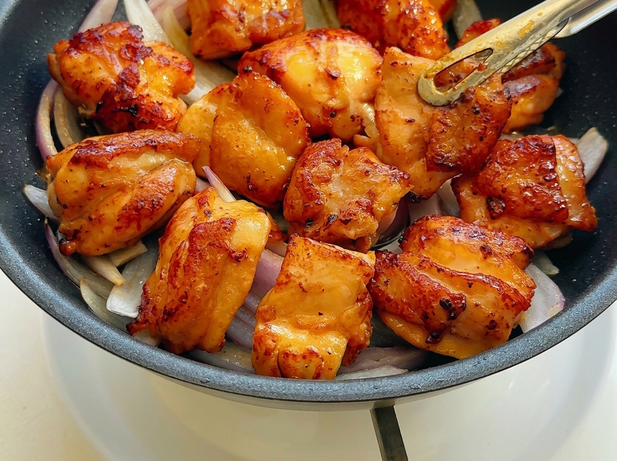 Pollo dorado colocado sobre las cebollas salteadas en la sartén.