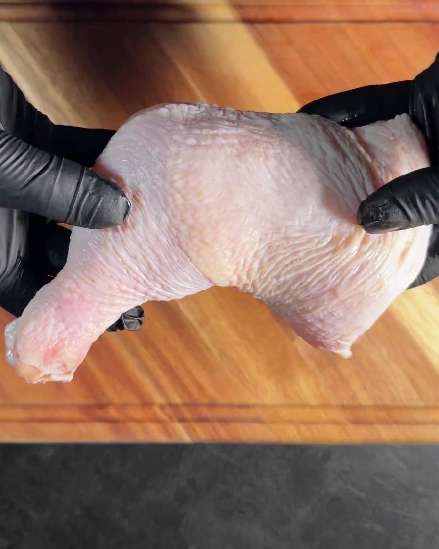 Un muslo de pollo deshuesado colocado plano sobre una tabla de cortar de madera.