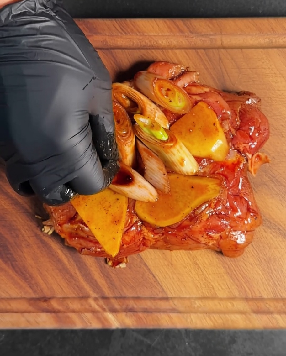 Los trozos de muslo de pollo cubiertos con el adobo y los aromáticos dentro de un bol de metal.
