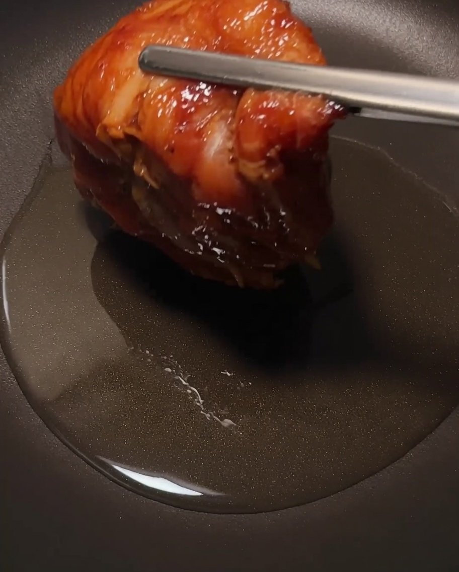 El muslo de pollo friéndose en una sartén, enfocándose en la piel crujiente.