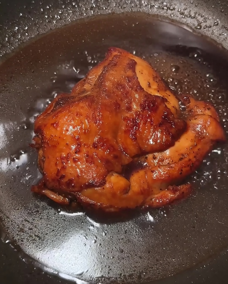 Una salsa oscura y sabrosa burbujeando en una sartén con trozos de pollo, volviéndose espesa y brillante tras añadir el almidón de maíz.