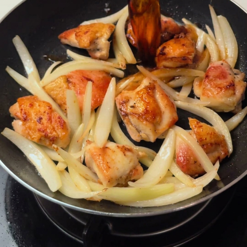 El pollo y las cebollas salteadas cocinándose a fuego lento en la sabrosa salsa a base de dashi dentro de la sartén.