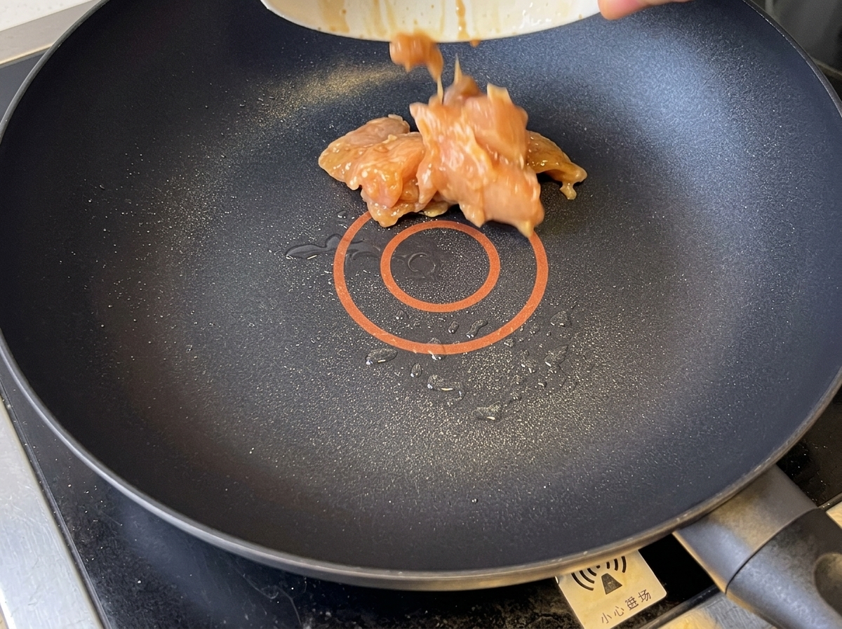 Trozos de pollo dorado siendo salteados en una sartén antiadherente.