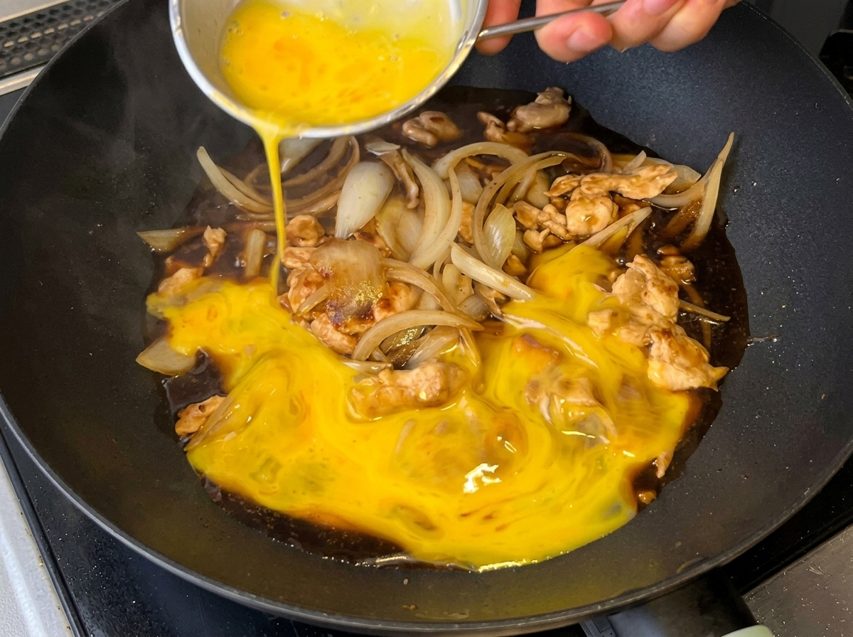Huevos batidos vertidos sobre la mezcla de pollo, cebolla y salsa en la sartén.