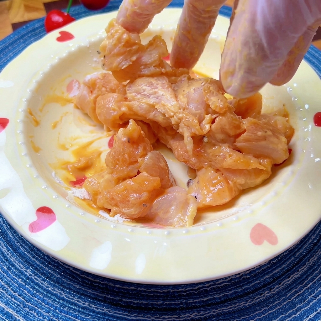 Trozos de pollo marinado siendo mezclados a mano en un cuenco.