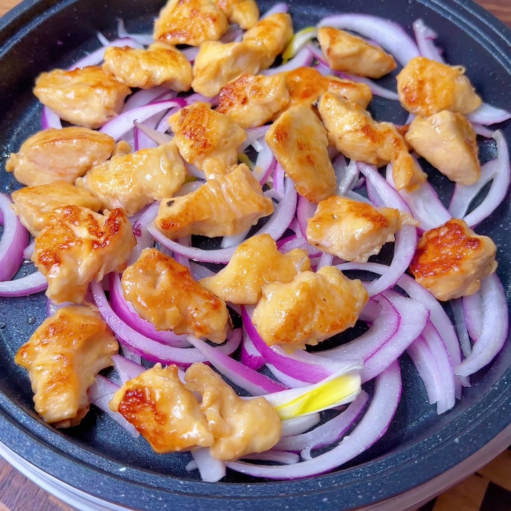 Pollo dorado y cebolla siendo cubiertos con la salsa sabrosa en la sartén.