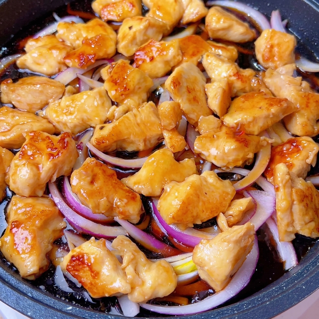 Una sartén tapada sobre el fuego, con la mezcla de pollo y cebolla cocinándose dentro.