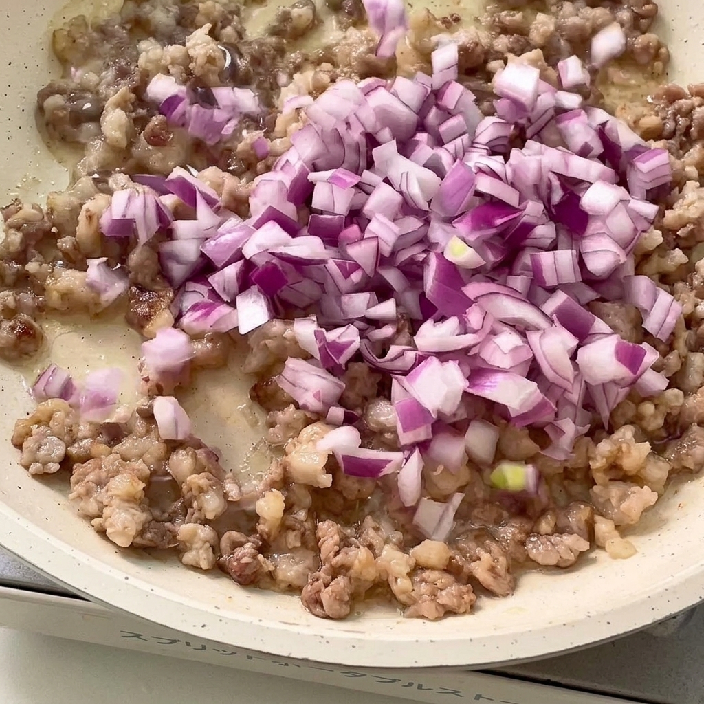 Cebolla morada picada y ajo siendo salteados con la carne dorada en la sartén.