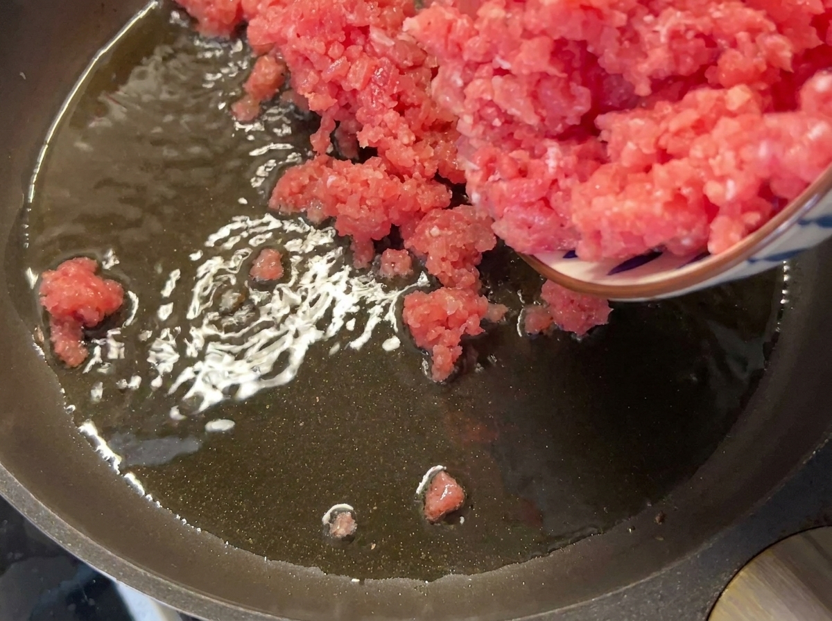 Cerdo magro picado siendo añadido a una sartén caliente con aceite.