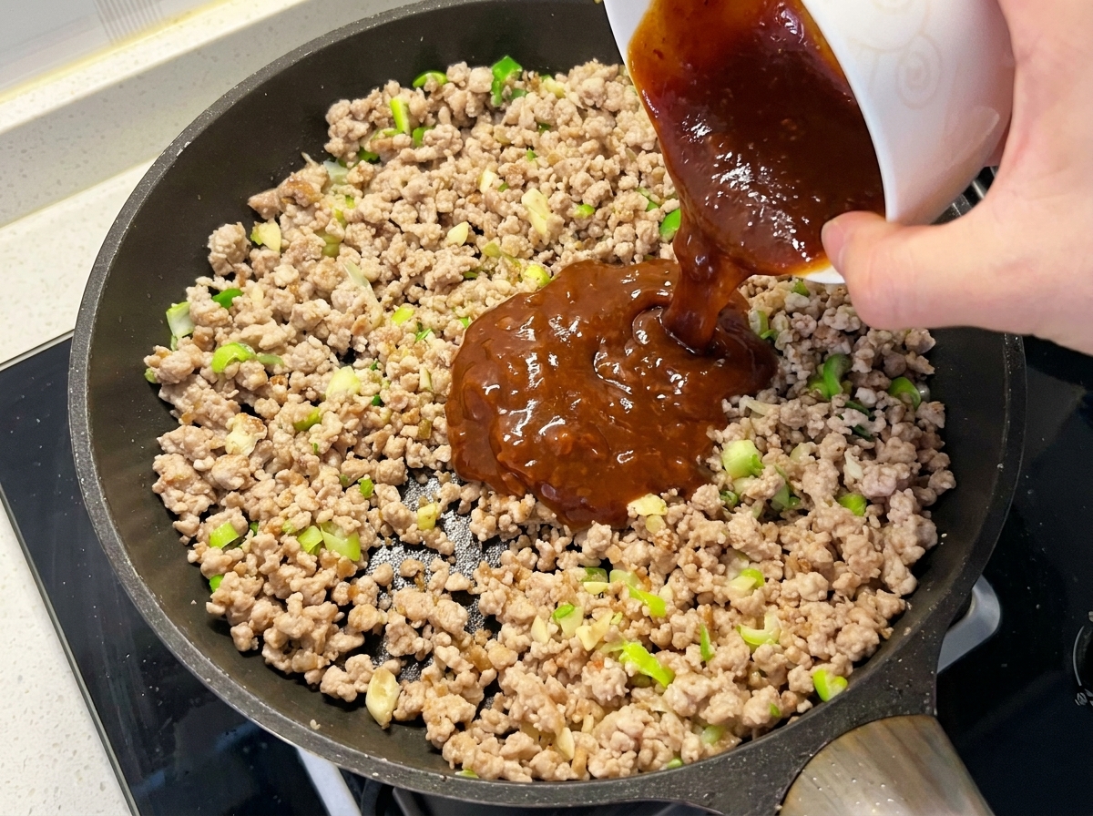 La mezcla de salsa siendo vertida en la sartén sobre la carne y los aromáticos.