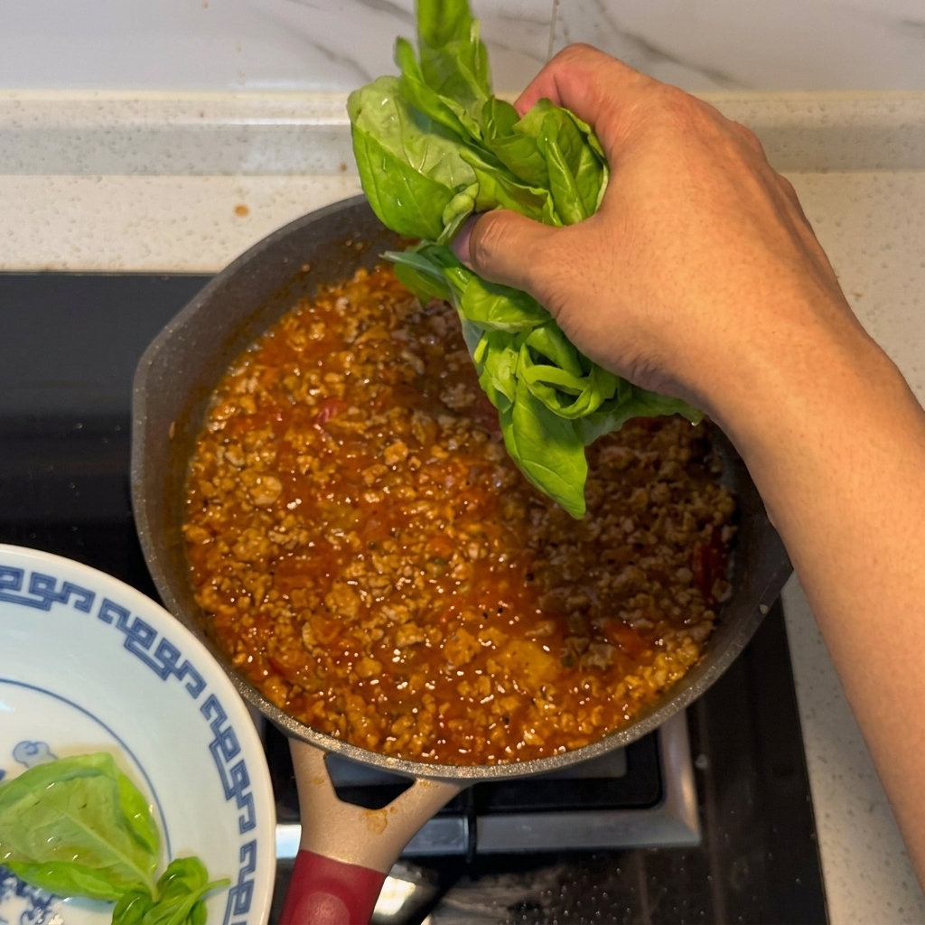Hojas de albahaca fresca siendo añadidas a la salsa terminada.