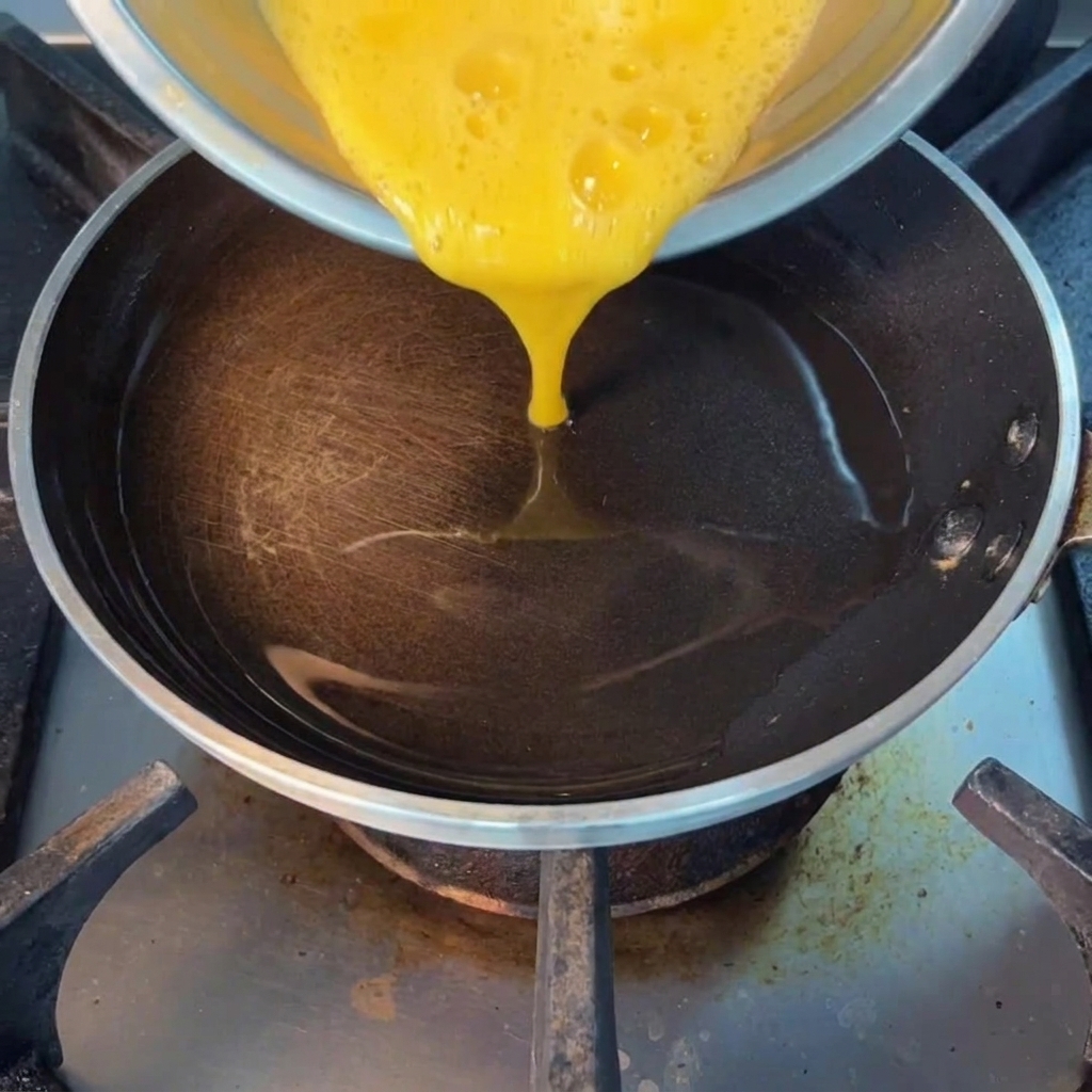 Huevos batidos siendo vertidos en una sartén caliente con aceite.