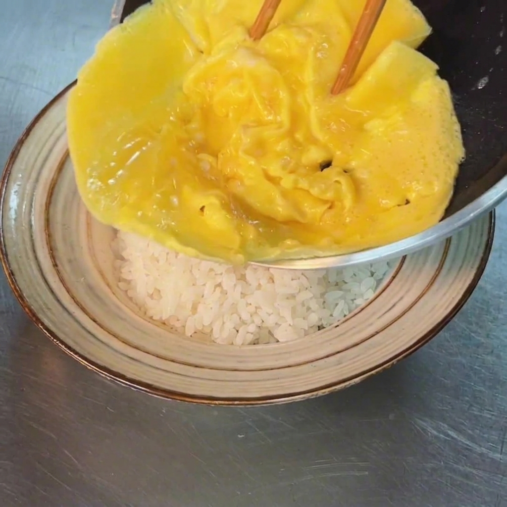 La tortilla suave siendo deslizada desde la sartén sobre un bowl de arroz blanco.
