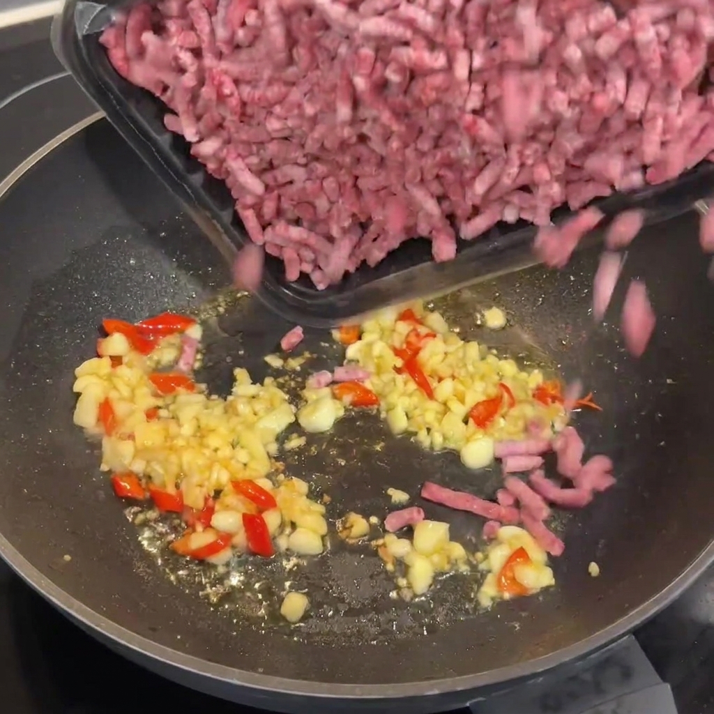 Carne picada de Wagyu cruda siendo añadida al wok caliente con los aromáticos salteados.