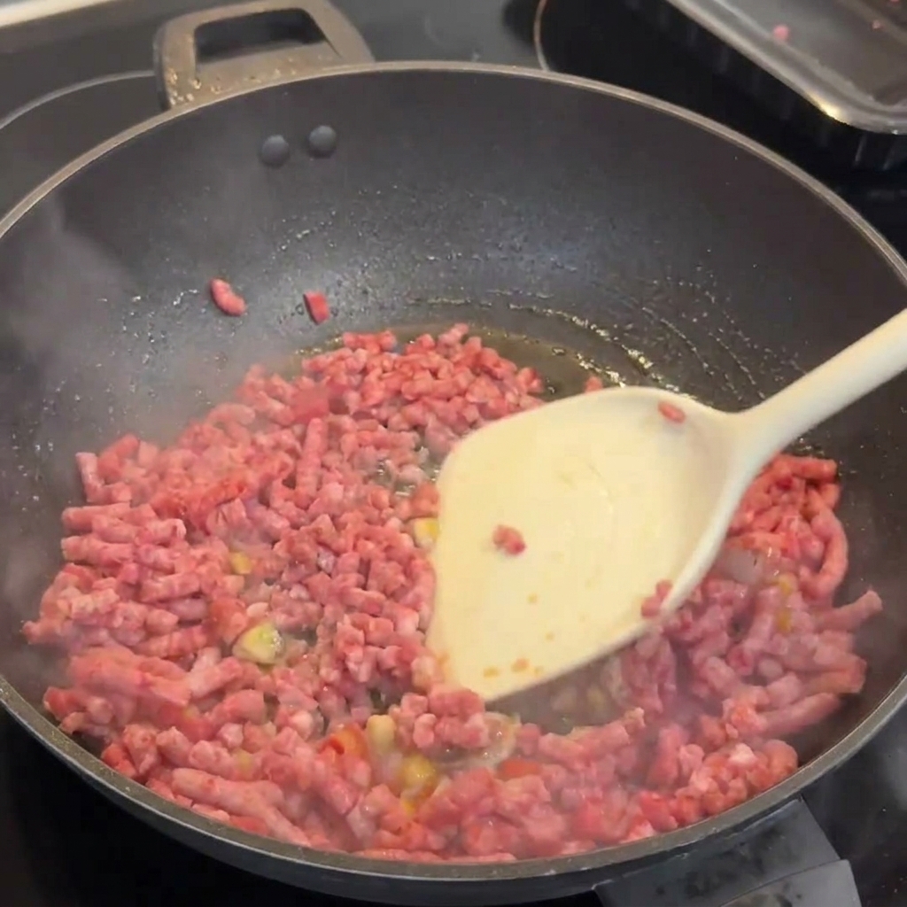 Carne picada de Wagyu dorándose en un wok con ajo y chiles, siendo separada con una espátula blanca.