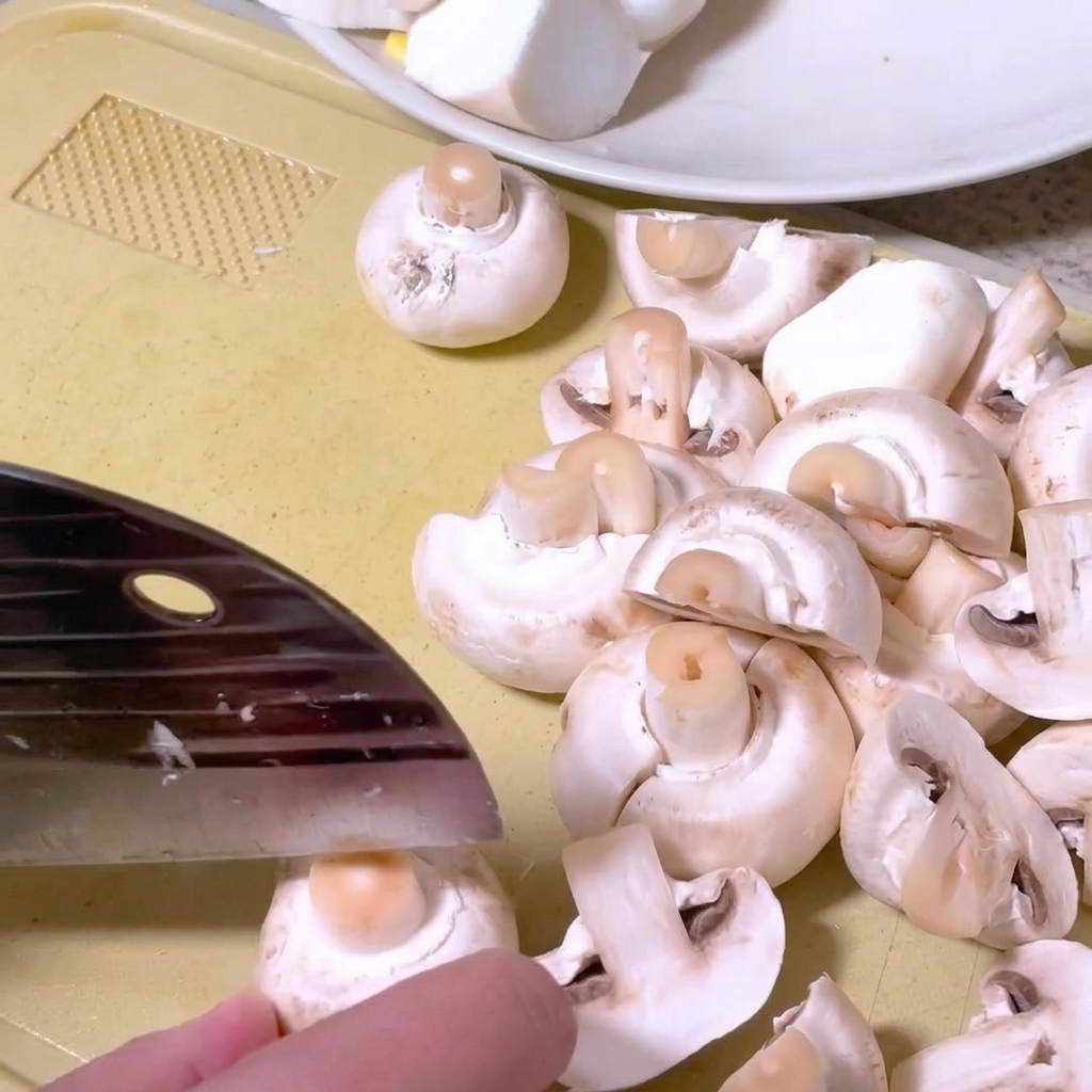 Champiñones siendo cortados por la mitad en una tabla de cortar con un cuchillo de cocina.