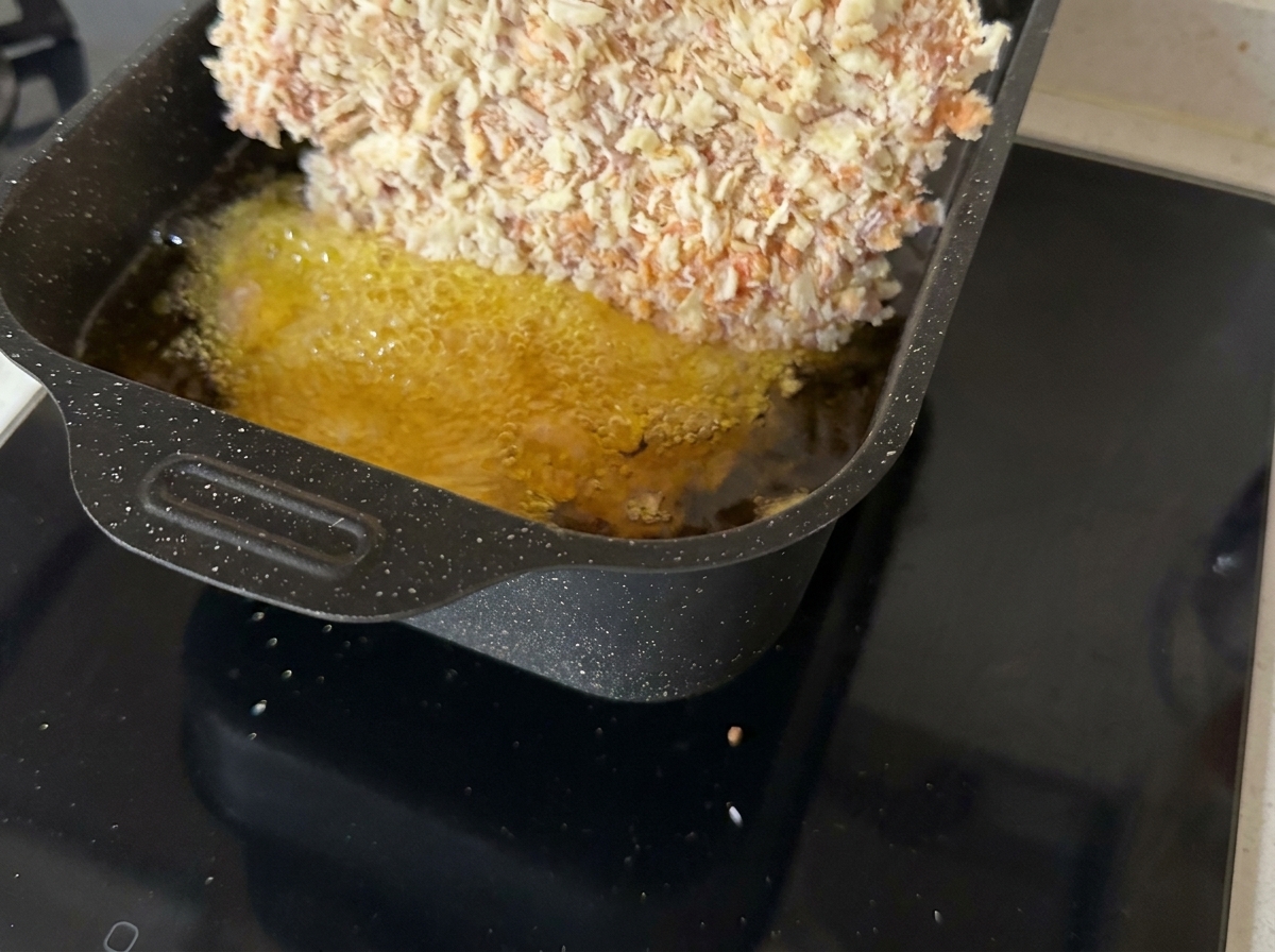 Una chuleta de ternera empanada friéndose en una sartén con aceite caliente burbujeante.