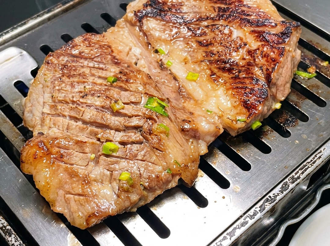 Primer plano de costillas de res al estilo coreano siendo cortadas en secciones más pequeñas con tijeras sobre una parrilla caliente.