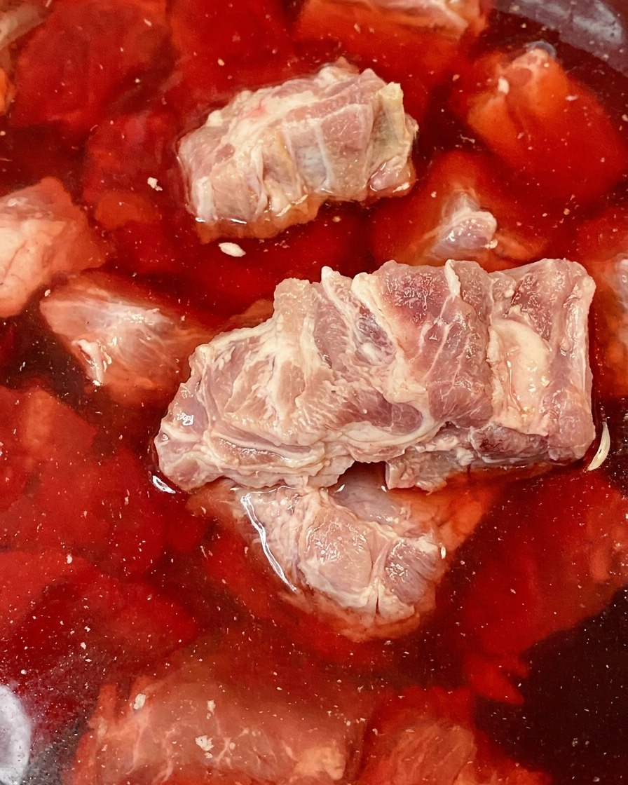 Espinazo de cerdo crudo sumergido en un tazón con agua teñida de rojo.