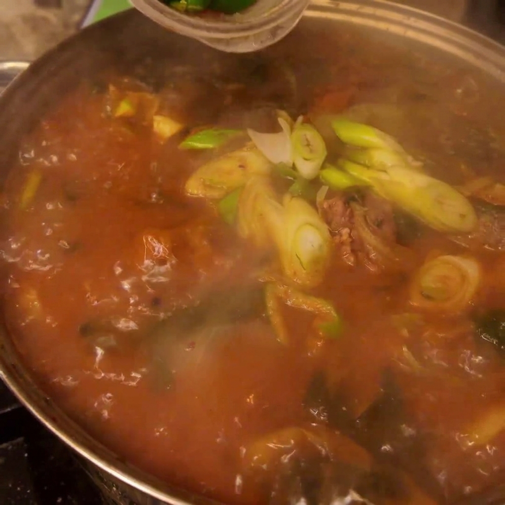 Chiles verdes y rojos frescos y cebollino siendo esparcidos sobre la olla de Gamjatang.