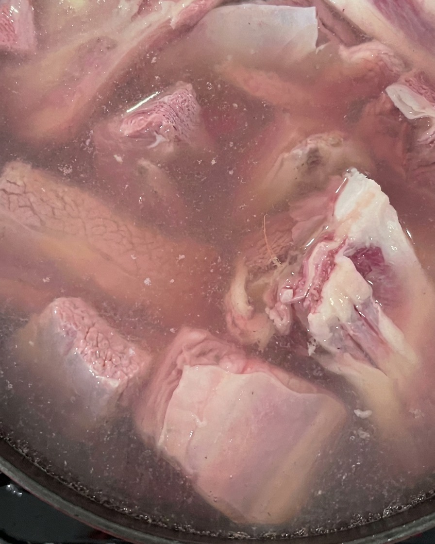 Costillas de ternera crudas y jengibre hirviendo en una olla con agua.