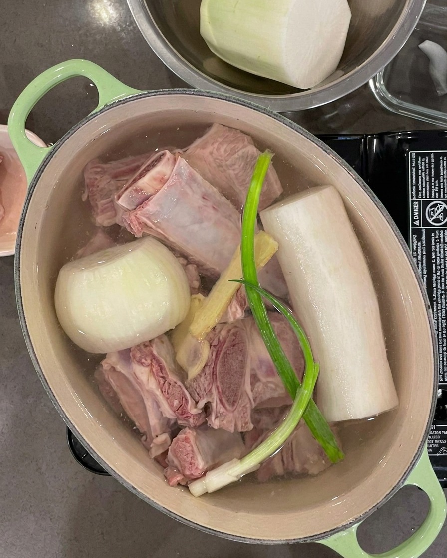 Agua siendo vertida en la olla, cubriendo completamente las costillas, los vegetales y los ingredientes aromáticos.