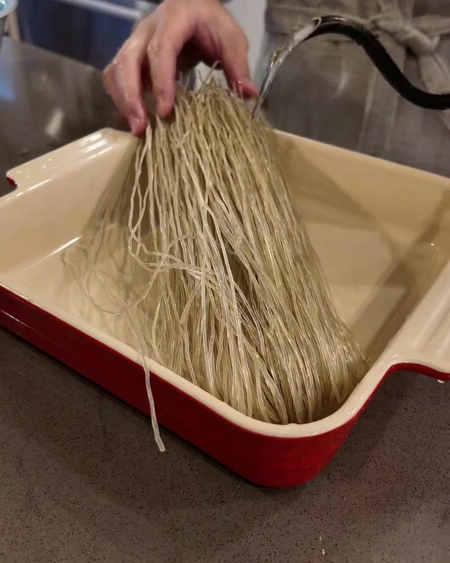 Fideos de cristal de camote secos remojándose en una fuente de horno llena de agua tibia.