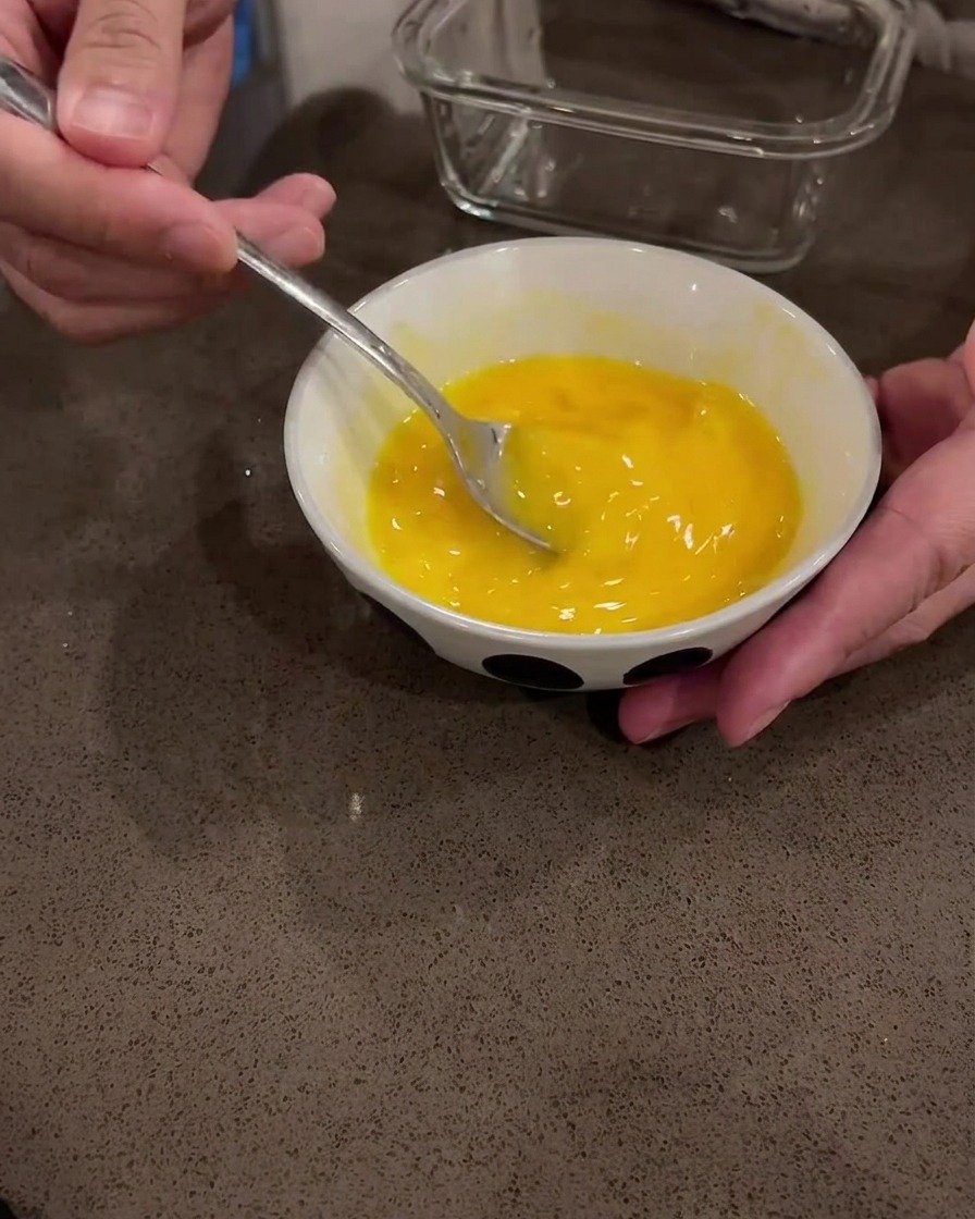 Huevos crudos siendo batidos en un tazón blanco con una cuchara de metal.