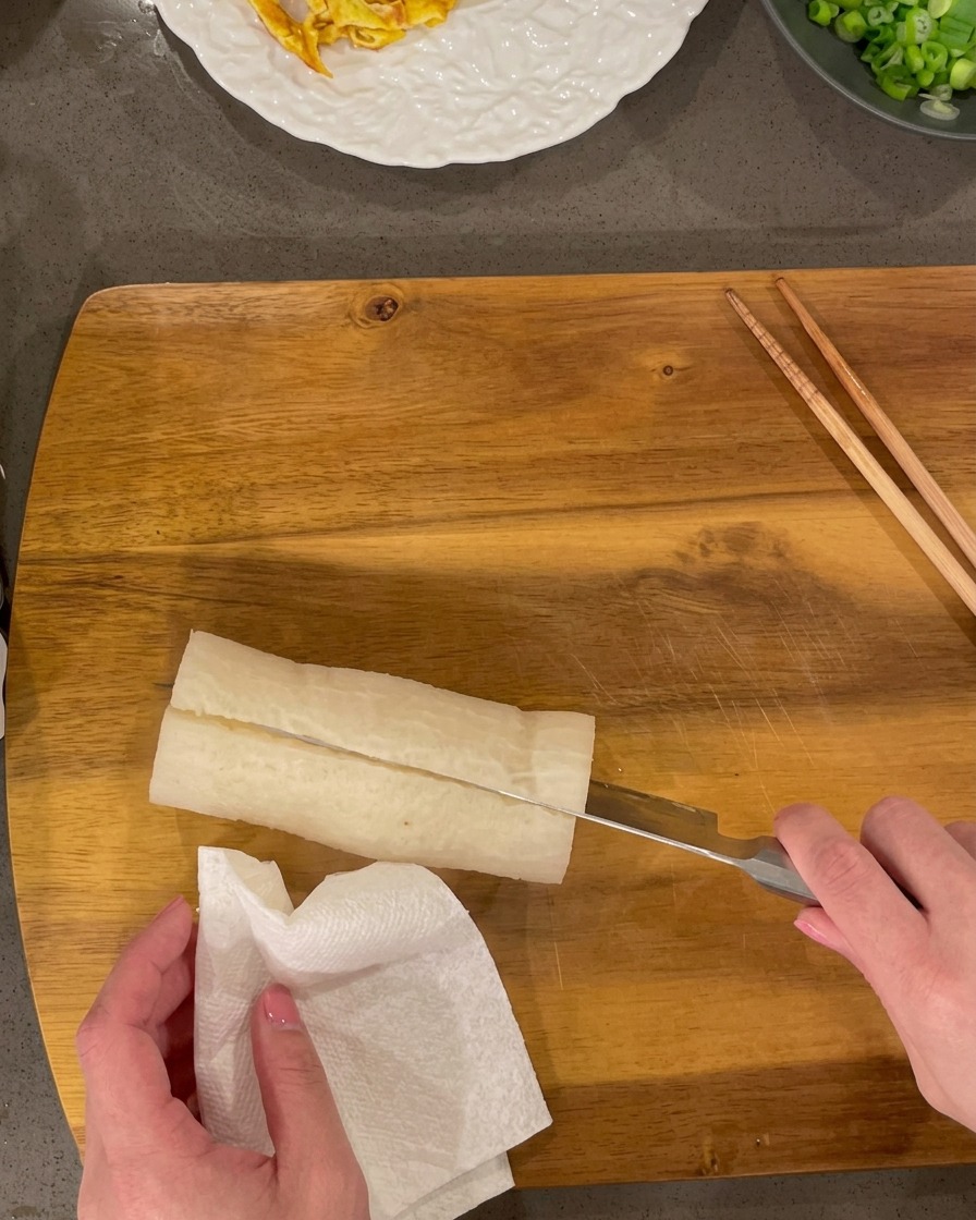 Rábano blanco cocido siendo cortado en pequeños rectángulos sobre una tabla de madera.